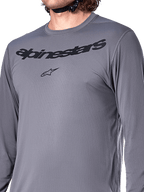 Jersey de manga larga Alpinestars A-Dura Rocker, gris oscuro, primer plano del pecho con la marca denominativa Alpinestars y el logotipo de la estrella en negro, material jacquard de poliéster y spandex, ropa de alto rendimiento para ciclismo de montaña