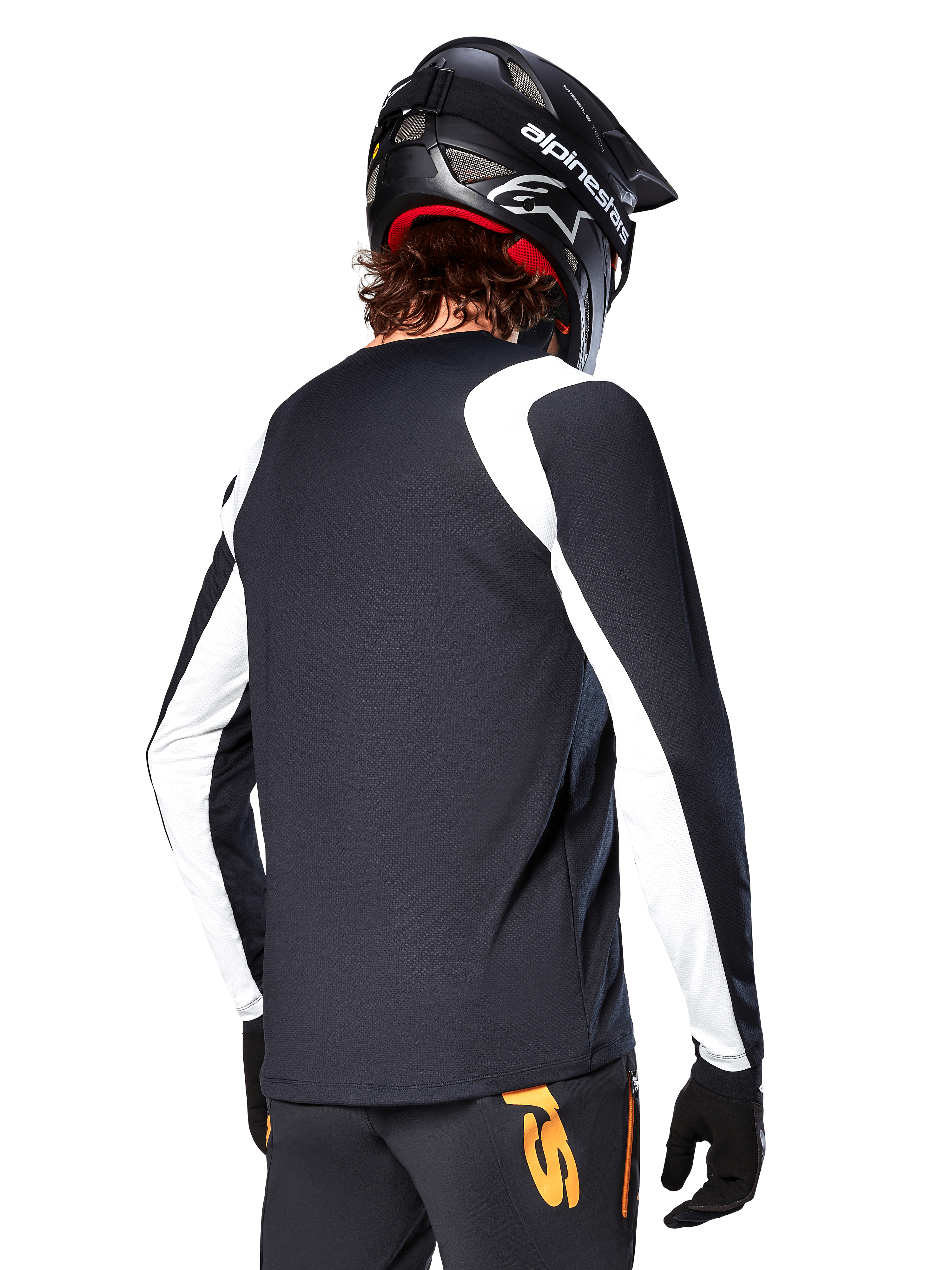Ciclista de MTB con el Jersey de Manga Larga Alpinestars A-Supra Oscar, negro con paneles blancos en los hombros y las mangas, visto desde atrás, casco y guantes negros, pantalones con detalles naranjas, ropa de ciclismo todoterreno duradera.