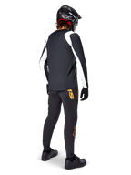 Jersey de manga larga Alpinestars A-Supra Oscar, negro con paneles blancos en las mangas, visto desde atrás en un ciclista de MTB con casco integral negro y pantalones negros con logotipos naranjas, ropa de ciclismo para gravity todoterreno