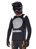 Alpinestars A-Supra Oscar Jersey de manga larga, jersey de ciclismo MTB, negro y blanco, con un llamativo diseño de espiral blanca y el logotipo de Alpinestars en el pecho, usado con un casco integral negro y gafas, ropa de ciclismo de montaña de alto rendimiento