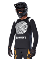 Alpinestars A-Supra Oscar Jersey de manga larga, jersey de ciclismo MTB, negro y blanco, con un llamativo diseño de espiral blanca y el logotipo de Alpinestars en el pecho, usado con un casco integral negro y gafas, ropa de ciclismo de montaña de alto rendimiento