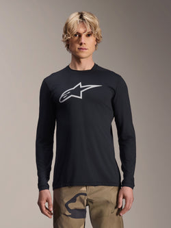 Jersey de manga larga Alpinestars A-Dura Astar, negro con logotipo plateado de Astars en el pecho, usado por un modelo con pantalones de camuflaje, ropa técnica casual para ciclismo de montaña MTB