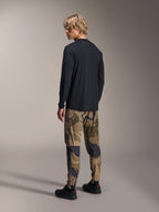 Alpinestars A-Dura Camo Pant, pantalones de MTB, camuflaje marrón, usados con un jersey negro de manga larga y zapatillas negras, vista trasera que muestra piernas ajustadas y puños elásticos, ropa técnica para ciclismo de montaña