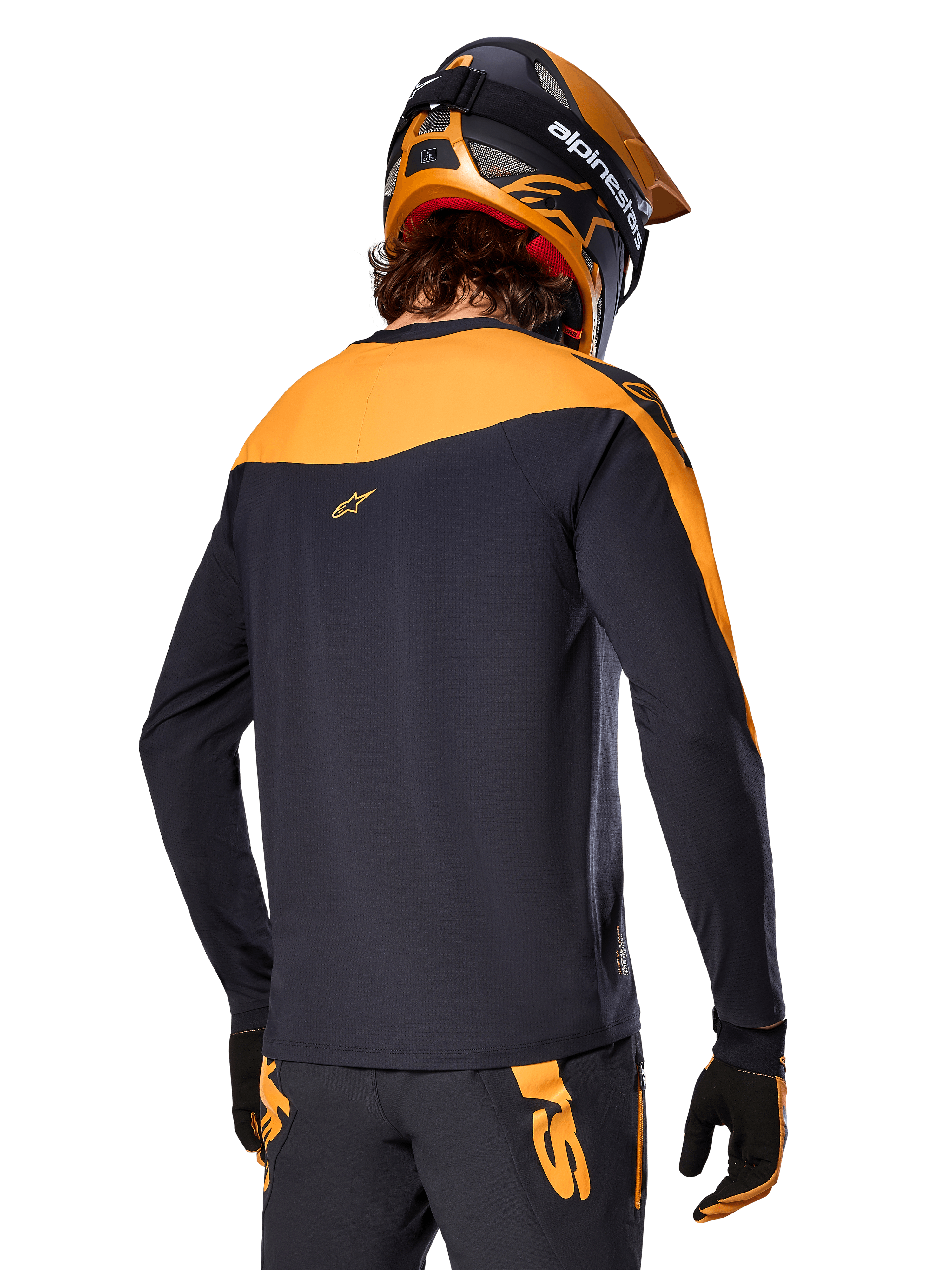 Alpinestars A-Supra Race Jersey de manga larga, negro y naranja, vista trasera del piloto con casco y pantalones de montaña a juego, ajuste de rendimiento con textura microperforada, equipo profesional para carreras de MTB