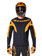 Ciclista de MTB con el jersey Alpinestars A-Supra Race de manga larga, negro con gráficos naranjas y logo en el pecho, combinado con un casco integral naranja a juego, gafas negras y guantes naranjas, kit de carreras coordinado para rendimiento en mountain bike