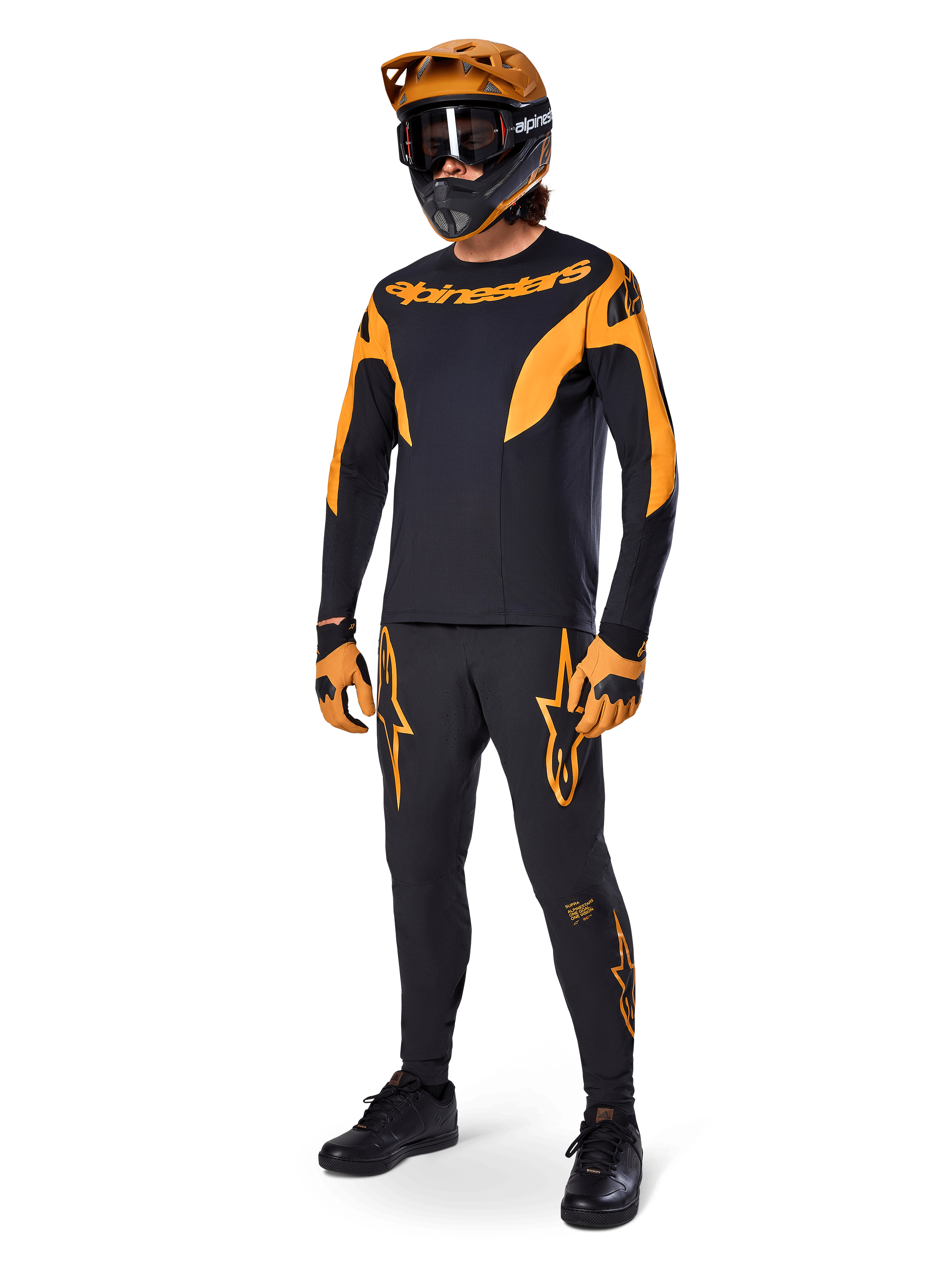 Ciclista de MTB con equipamiento completo de competición, jersey A-Supra Race negro con detalles en naranja, pantalones negros a juego con logotipos de Alpinestars en naranja, casco integral naranja y negro con gafas, guantes naranjas y negros, conjunto coordinado para carreras de bicicleta de montaña