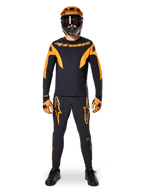 Ciclista de MTB con el Jersey Alpinestars A-Supra Race de manga larga en negro y naranja, pantalones, guantes y casco integral con gafas a juego, conjunto coordinado de ciclismo de montaña para competición y rendimiento off-road