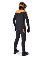 Jersey A-Supra Race de manga larga, negro y naranja, vista trasera de un piloto con pantalones de MTB a juego, casco naranja y negro, y guantes, equipamiento de alto rendimiento para carreras de mountain bike