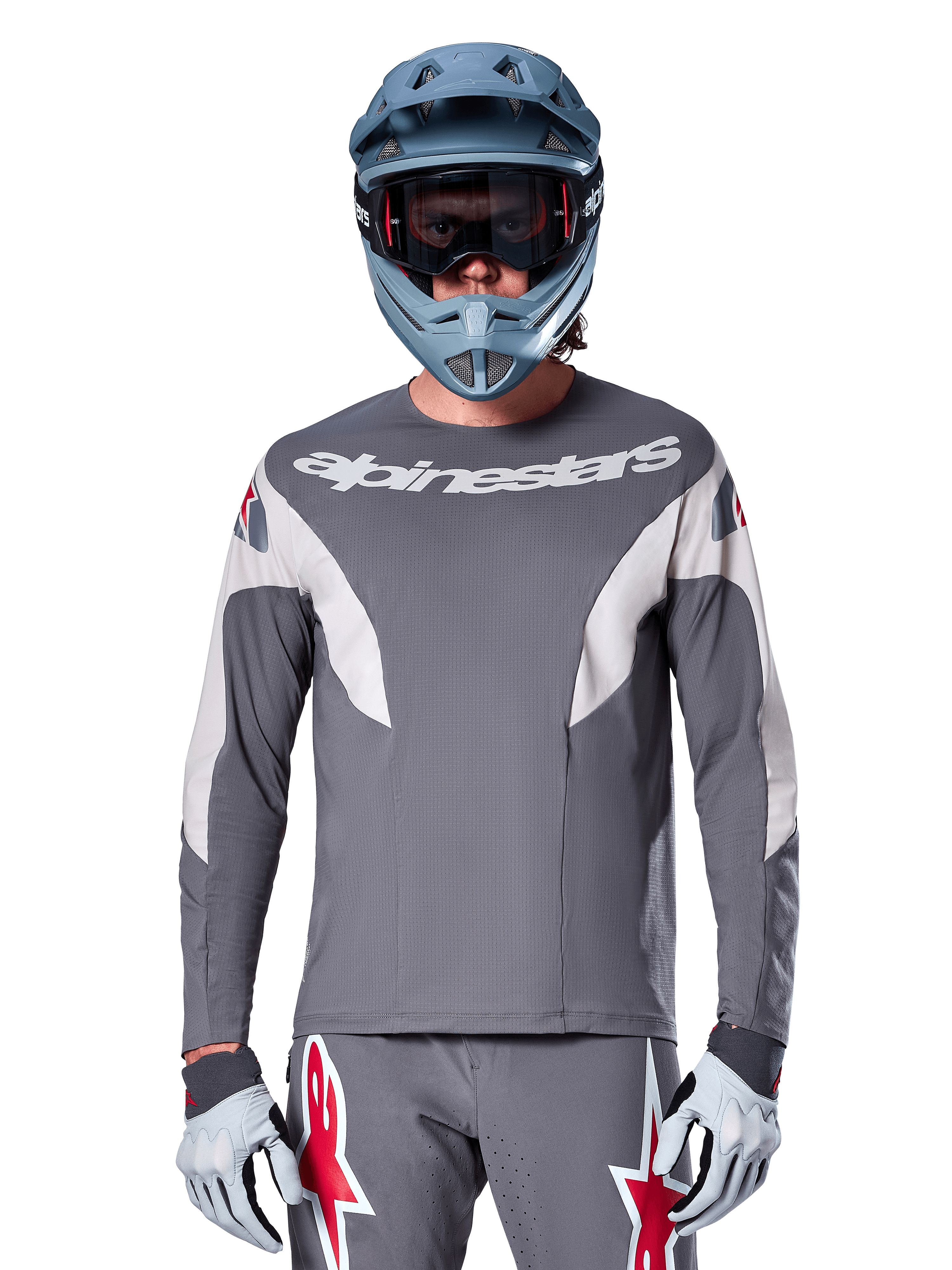 Ciclista de MTB vistiendo el Jersey Alpinestars A-Supra Race - Manga Larga en gris oscuro, jersey de ciclismo de manga larga con marca Alpinestars en blanco, combinado con un casco integral gris azulado, gafas y guantes de carreras grises, equipo completo de carreras de bicicleta de montaña para rendimiento todoterreno