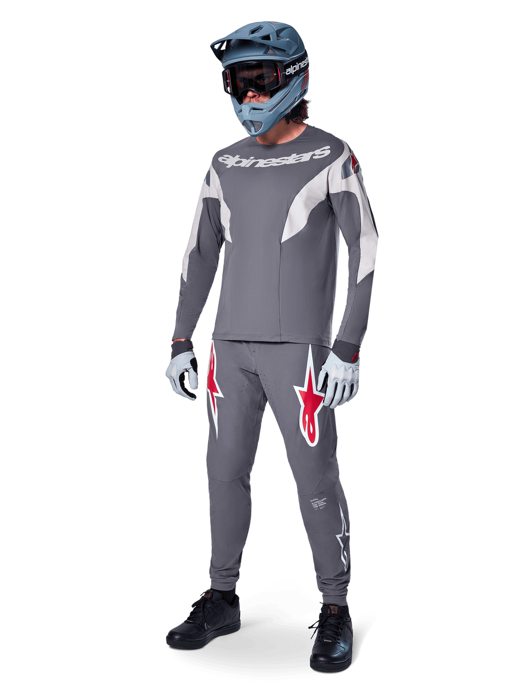 Ciclista de MTB con el Jersey Alpinestars A-Supra Race de manga larga, gris oscuro con detalles en gris claro, pantalones a juego con el logo de la estrella roja, casco integral gris con gafas y guantes gris claro, equipamiento coordinado para carreras de mountain bike