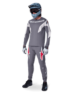 Ciclista de MTB con el Jersey Alpinestars A-Supra Race de manga larga, gris oscuro con detalles en gris claro, pantalones a juego con el logo de la estrella roja, casco integral gris con gafas y guantes gris claro, equipamiento coordinado para carreras de mountain bike