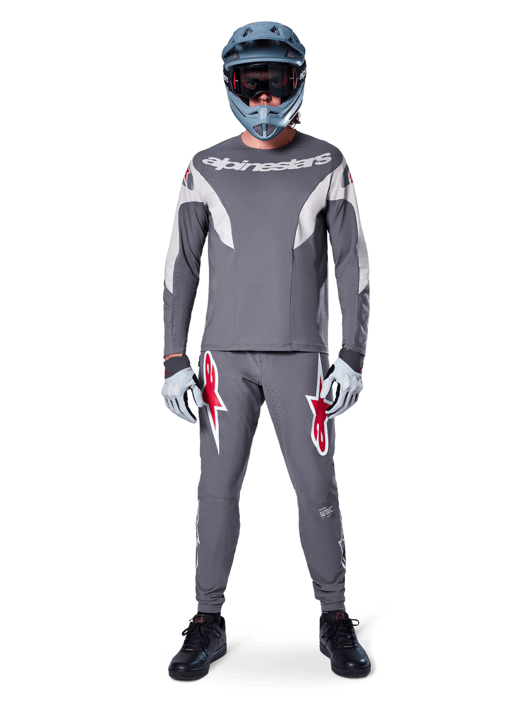 Piloto con el jersey de manga larga Alpinestars A-Supra Race en gris oscuro, combinado con pantalones grises a juego con llamativos logotipos de estrella rojos, casco gris con gafas y guantes gris claro, equipamiento completo de competición de MTB para ciclismo de montaña de alto rendimiento