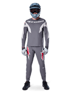 Piloto con el jersey de manga larga Alpinestars A-Supra Race en gris oscuro, combinado con pantalones grises a juego con llamativos logotipos de estrella rojos, casco gris con gafas y guantes gris claro, equipamiento completo de competición de MTB para ciclismo de montaña de alto rendimiento