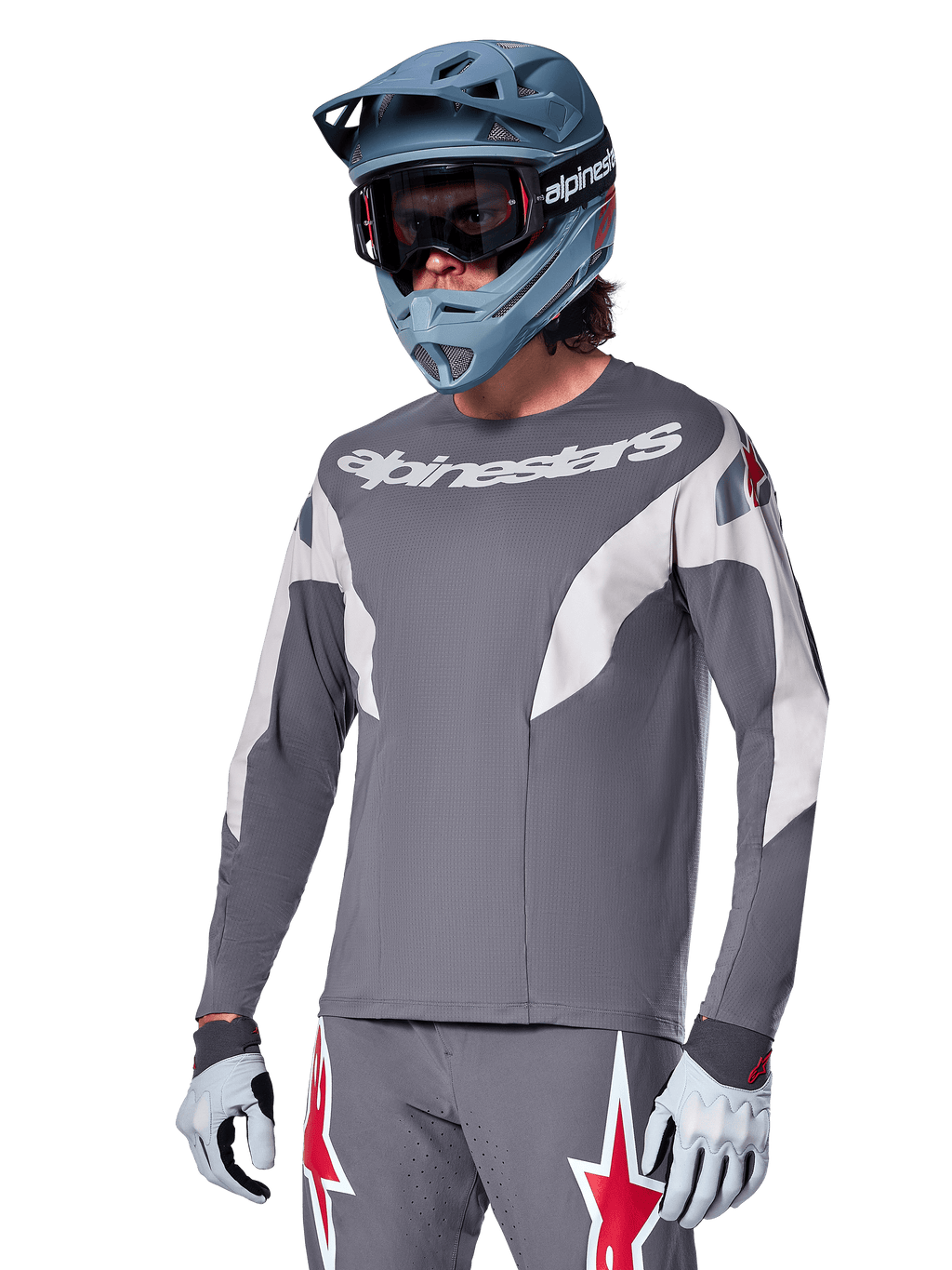 Alpinestars A-Supra Race Jersey de manga larga, gris oscuro con detalles blancos y rojos, gráficos de estilo de carreras, usado con pantalones grises a juego, casco integral azul y guantes blancos, equipo profesional de MTB y descenso