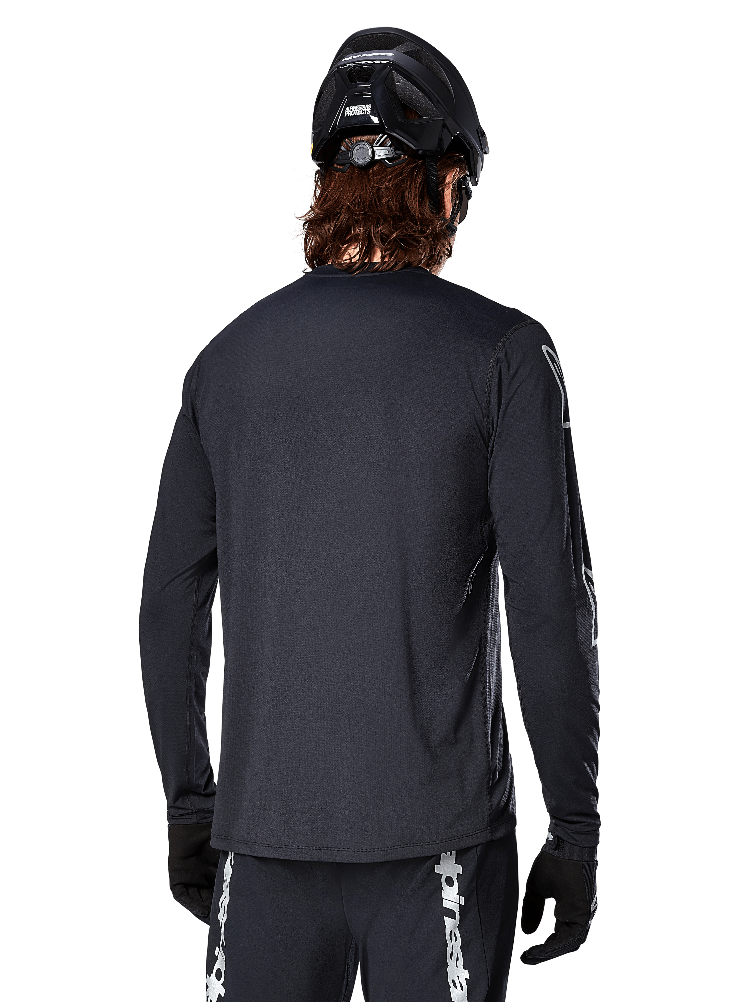 Jersey de manga larga Alpinestars A-Dura Switch, negro, vista trasera de un ciclista con casco de MTB y guantes negros, con tejido jacquard técnico y parte trasera más larga para conducción off-road