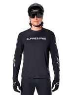 Jersey de manga larga Alpinestars A-Dura Switch, jersey de MTB negro, logotipo de Alpinestars en blanco en el pecho y gráficos de estrellas en las mangas, usado con casco de bicicleta de montaña negro y gafas de sol de alto rendimiento, ropa técnica para trail
