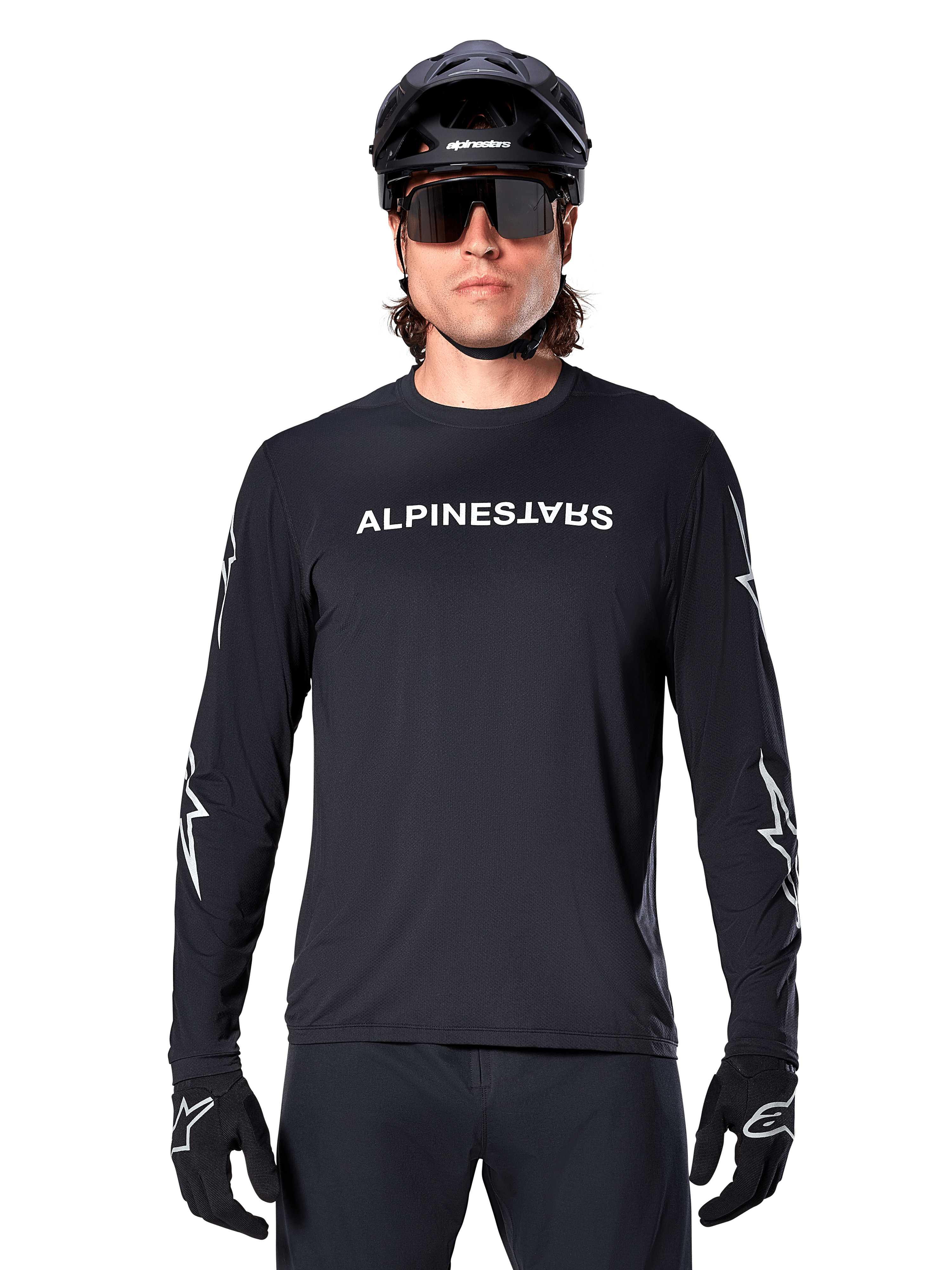 Jersey de manga larga Alpinestars A-Dura Switch, jersey de MTB negro, logotipo de Alpinestars en blanco en el pecho y gráficos de estrellas en las mangas, usado con casco de bicicleta de montaña negro y gafas de sol de alto rendimiento, ropa técnica para trail