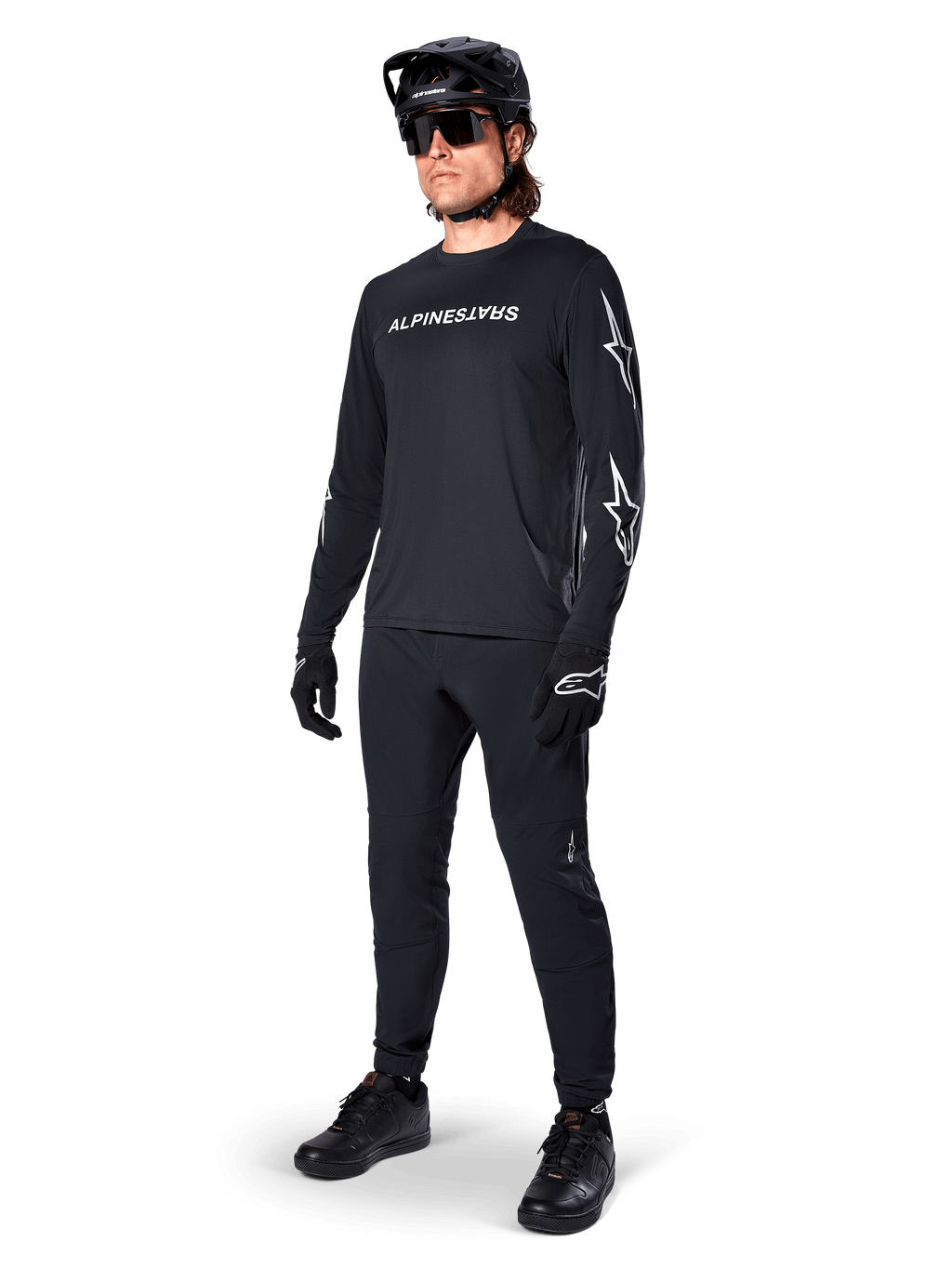 Alpinestars A-Dura Switch Long Sleeve Jersey, negro, jersey de bicicleta de montaña usado con pantalones negros, casco y guantes, con logotipo de marca blanco en el pecho y logotipos de estrella en las mangas, equipamiento de MTB coordinado para conducción todoterreno