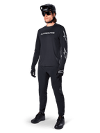 Alpinestars A-Dura Switch Long Sleeve Jersey, negro, jersey de bicicleta de montaña usado con pantalones negros, casco y guantes, con logotipo de marca blanco en el pecho y logotipos de estrella en las mangas, equipamiento de MTB coordinado para conducción todoterreno