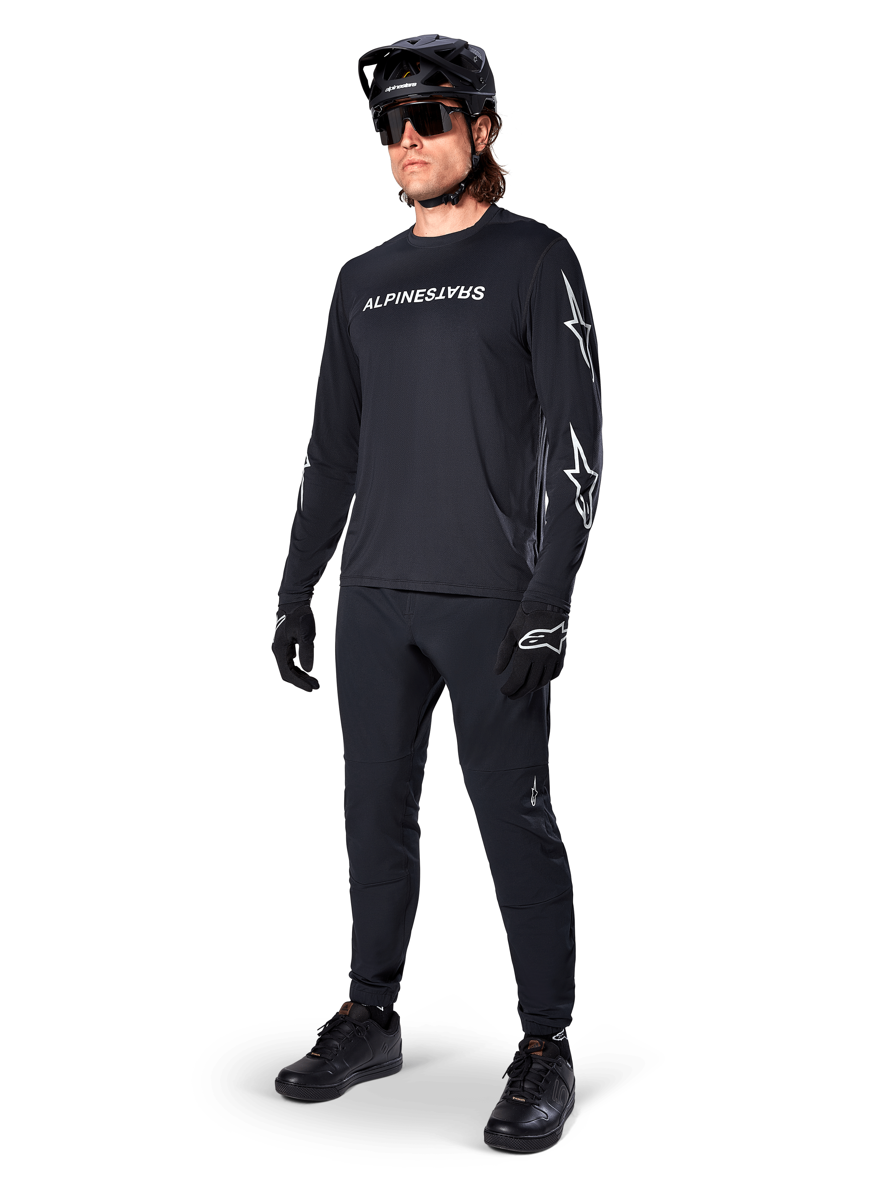 Alpinestars A-Dura Switch Long Sleeve Jersey, negro, jersey de bicicleta de montaña usado con pantalones negros, casco y guantes, con logotipo de marca blanco en el pecho y logotipos de estrella en las mangas, equipamiento de MTB coordinado para conducción todoterreno