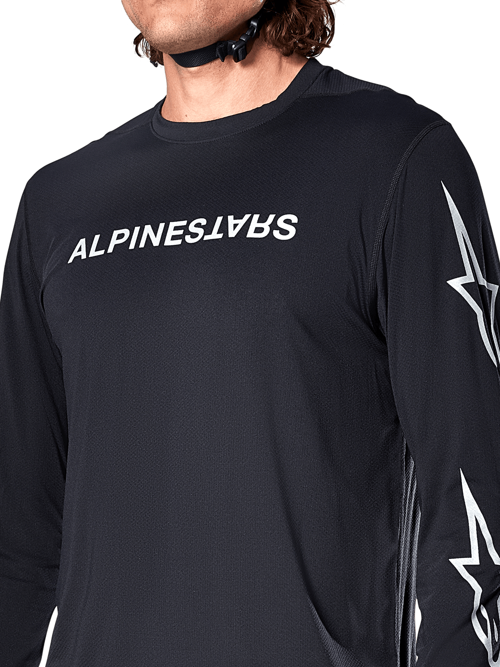 Jersey de manga larga Alpinestars A-Dura Switch, negro, con el logotipo de Alpinestars en blanco en el pecho y estrellas en la manga, usado por un ciclista con la correa del casco visible, ropa técnica para bicicleta de montaña
