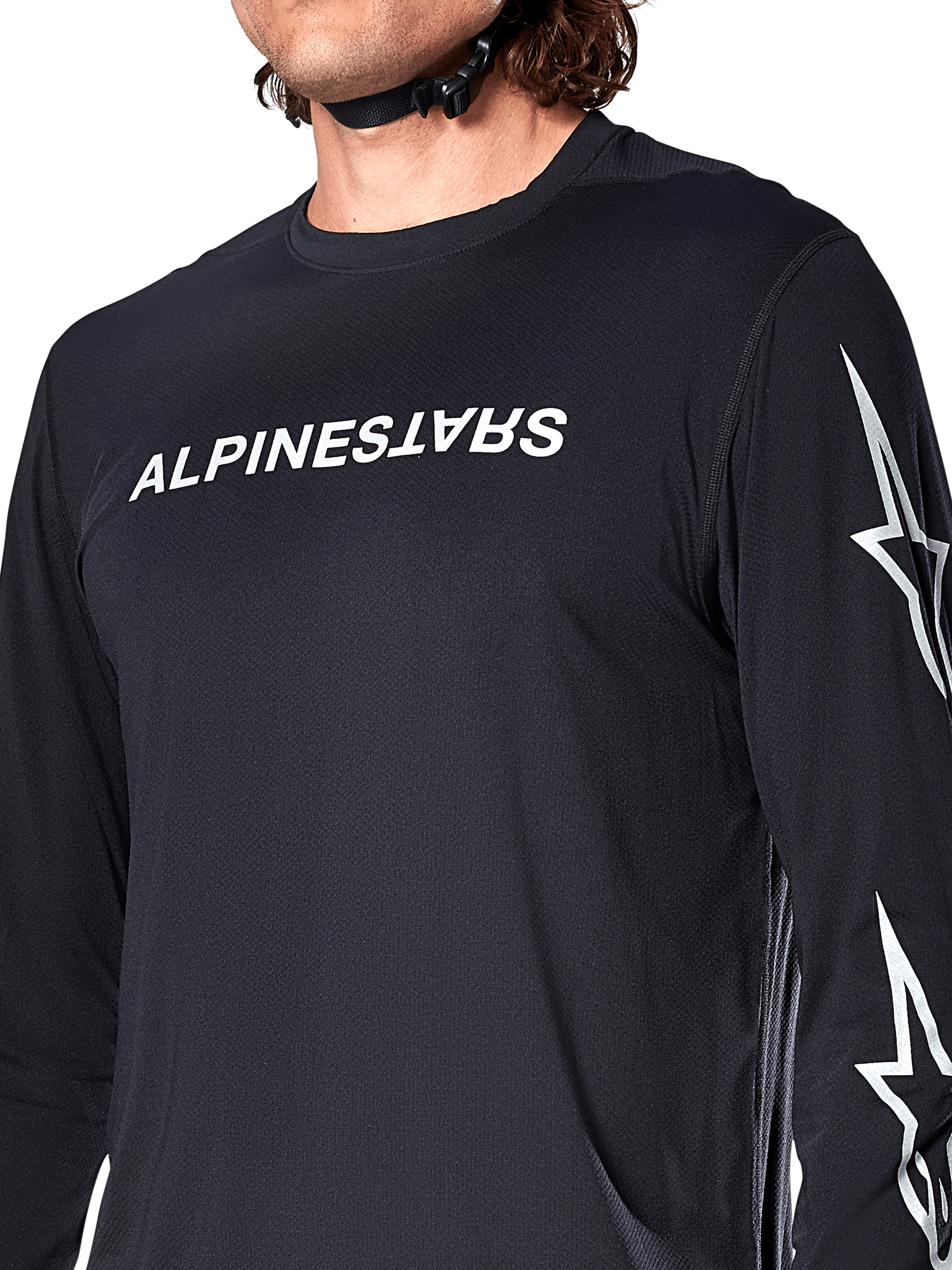 Jersey de manga larga Alpinestars A-Dura Switch, negro, con el logotipo de Alpinestars en blanco en el pecho y estrellas en la manga, usado por un ciclista con la correa del casco visible, ropa técnica para bicicleta de montaña