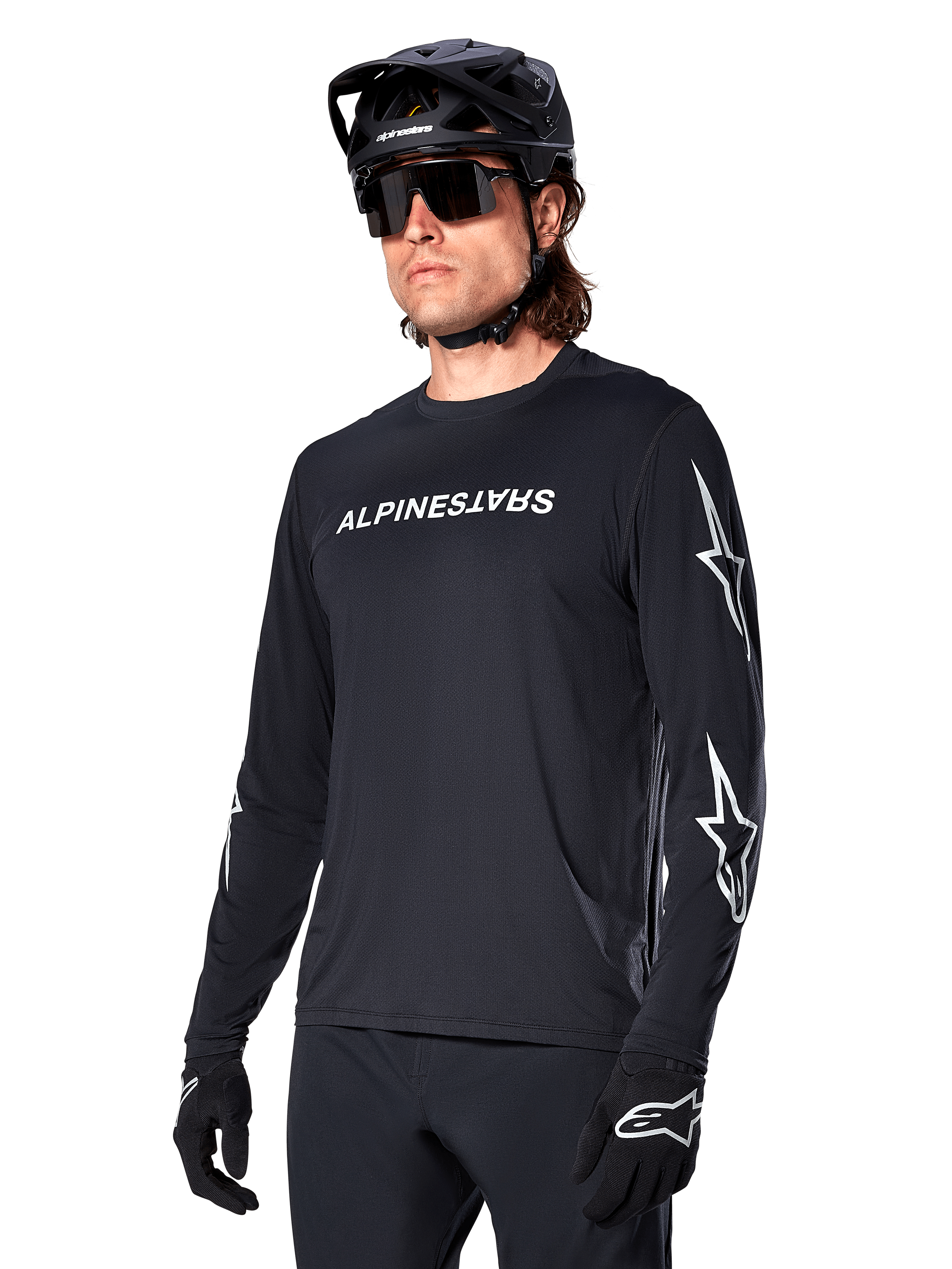 Ciclista masculino con jersey de manga larga Alpinestars A-Dura Switch, negro con marca en blanco y logotipos de estrella en las mangas, combinado con casco de MTB negro y gafas de sol, equipamiento de ciclismo de alto rendimiento para rutas todoterreno
