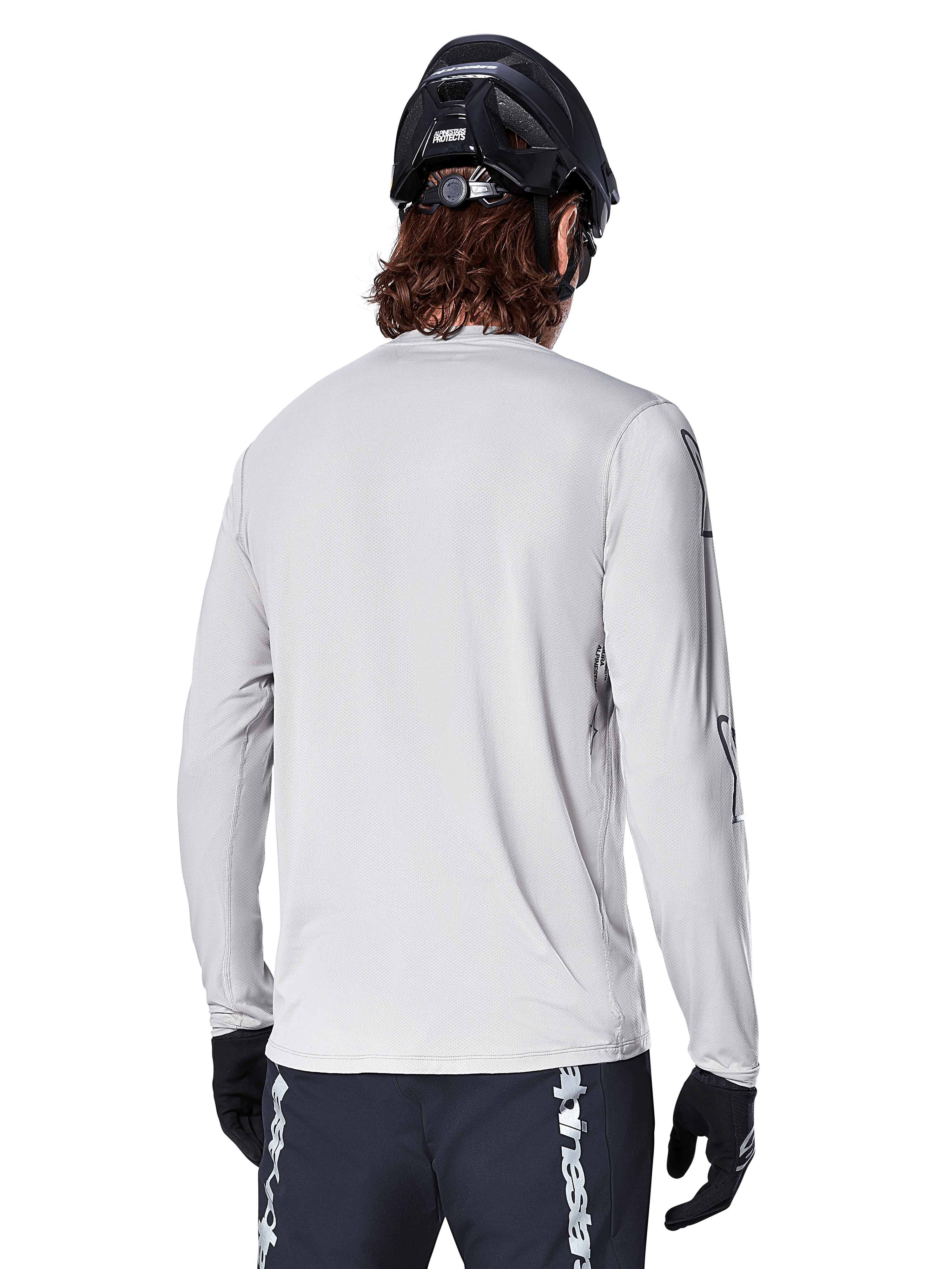 Jersey de manga larga Alpinestars A-Dura Switch, Gris Claro, vista trasera de un ciclista de montaña con casco de MTB negro y guantes, con una parte trasera más larga para mayor cobertura y tejido jacquard texturizado, equipamiento de ciclismo de alto rendimiento.