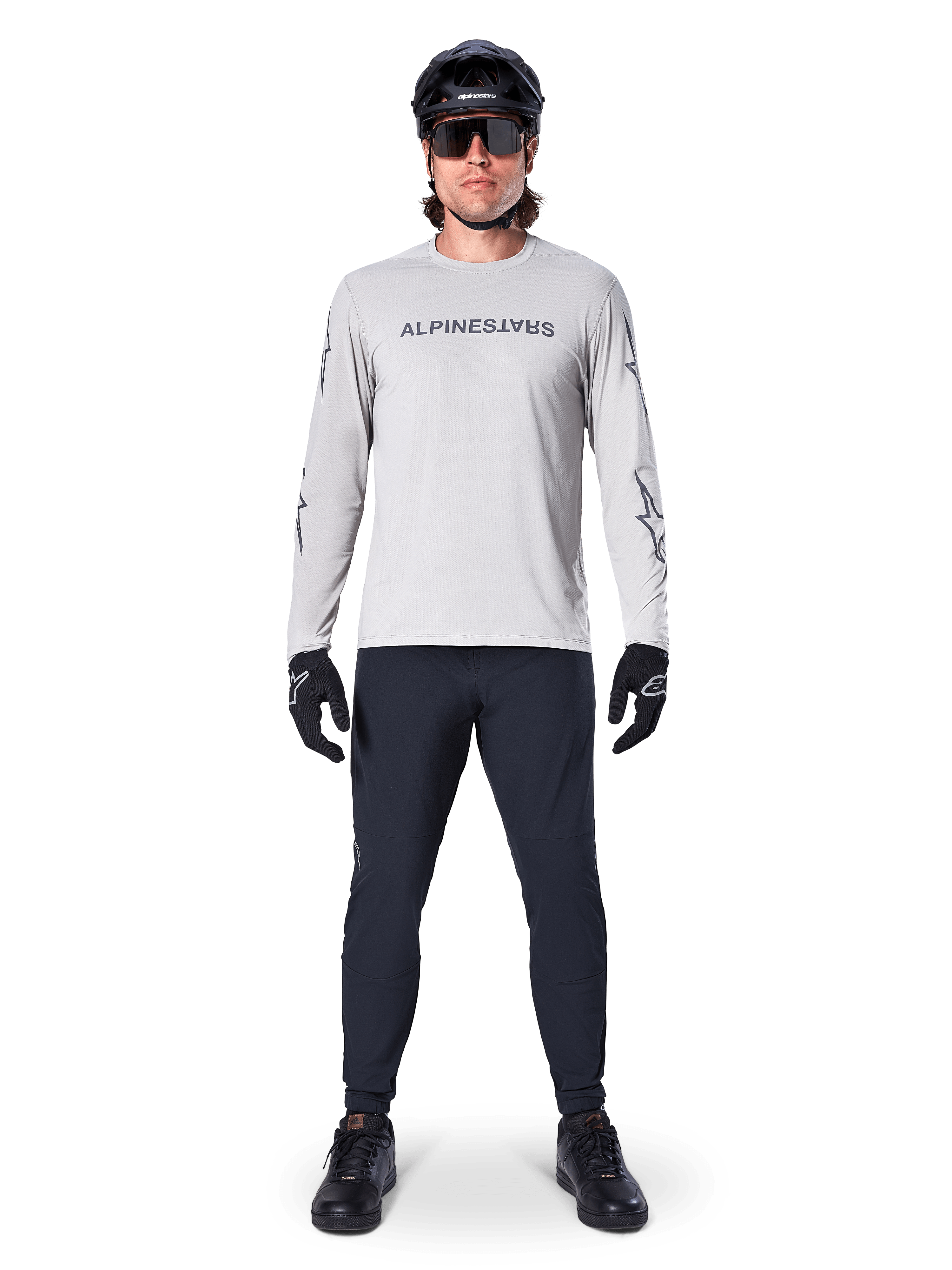 Jersey de manga larga Alpinestars A-Dura Switch en gris claro, con un logotipo estilizado en el pecho, combinado con pantalones negros, casco y guantes, ropa de alto rendimiento para ciclismo de montaña fuera de pista