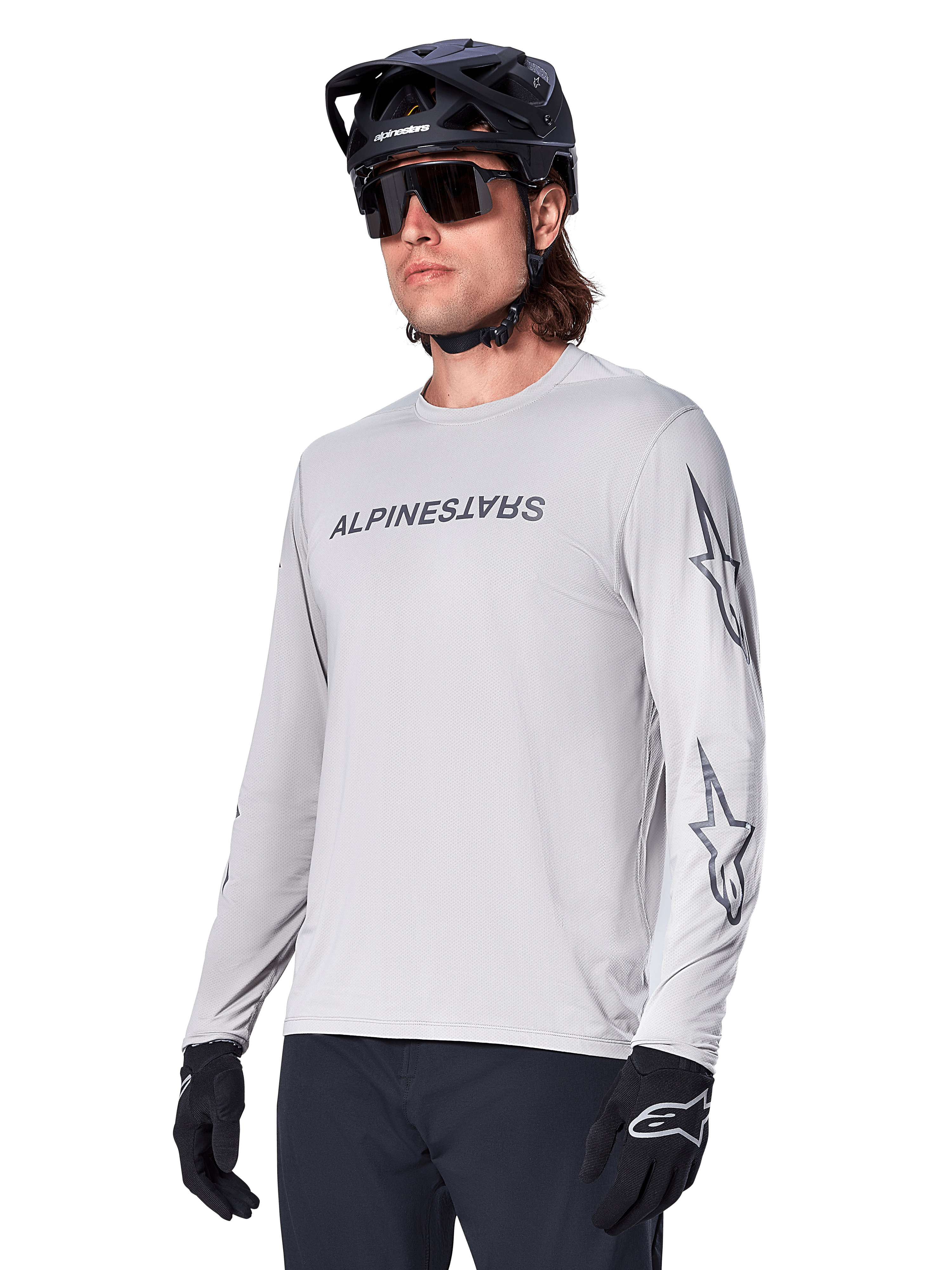 Alpinestars A-Dura Switch Long Sleeve Jersey, camiseta de manga larga para bicicleta de montaña, gris claro, serigrafía negra de la marca en el pecho y logotipos de estrellas en las mangas, usado con casco negro de MTB, gafas de sol oscuras y guantes negros, equipamiento deportivo para ciclismo off-road