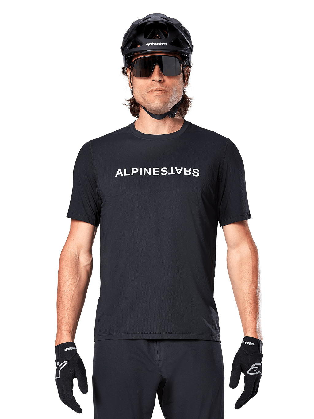 Ciclista de montaña con el jersey de manga corta Alpinestars A-Dura Switch en color negro, con un logotipo de la marca en blanco en el pecho, combinado con casco negro, gafas de sol grandes y guantes negros, ropa de ciclismo profesional para trail.