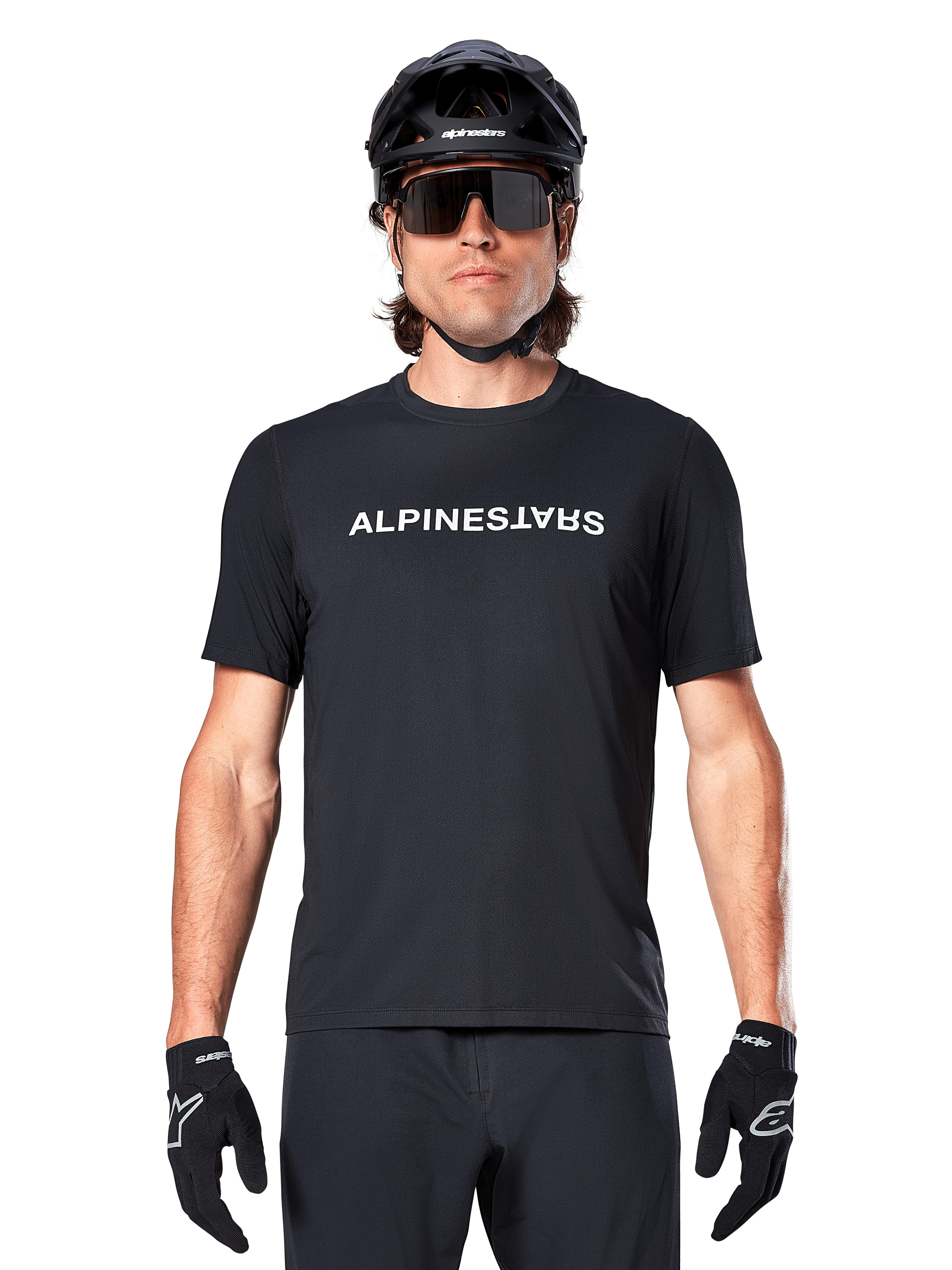 Ciclista de montaña con el jersey de manga corta Alpinestars A-Dura Switch en color negro, con un logotipo de la marca en blanco en el pecho, combinado con casco negro, gafas de sol grandes y guantes negros, ropa de ciclismo profesional para trail.