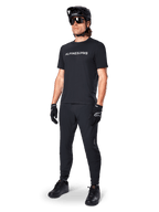 Camiseta de manga corta Alpinestars A-Dura Switch, negra, vestida por un modelo con pantalones de MTB, casco y guantes negros a juego, con el logotipo de Alpinestars en blanco sobre el pecho, ropa de alto rendimiento para ciclismo de montaña