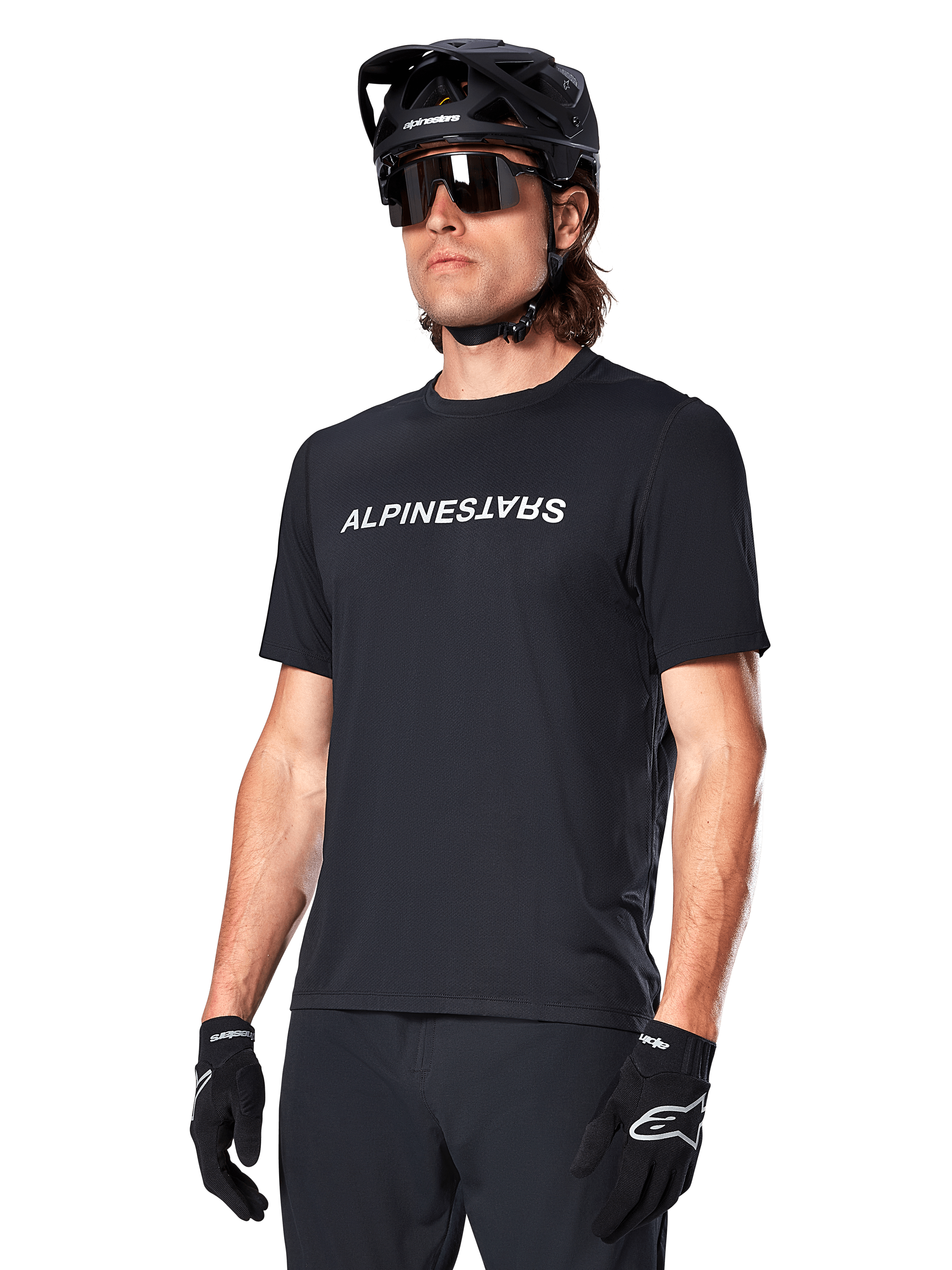 Jersey Alpinestars A-Dura Switch de manga corta, negro, con un logotipo blanco de la marca en el pecho, usado por un ciclista con casco de MTB negro y gafas de sol, ropa técnica diseñada para ciclismo de montaña
