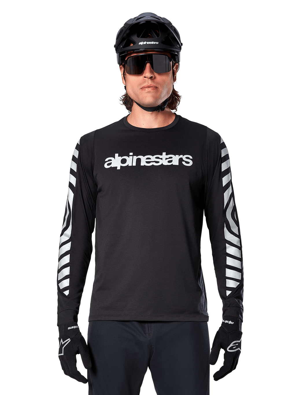 Ciclista masculino con jersey de manga larga Alpinestars A-Dura Dri Oscar, Negro Reflectante, con logotipo de Alpinestars en blanco en el pecho y gráficos reflectantes plateados en las mangas, combinado con casco de MTB negro, gafas de sol y guantes negros, equipamiento de ciclismo de alto rendimiento