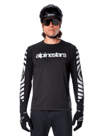 Ciclista masculino con jersey de manga larga Alpinestars A-Dura Dri Oscar, Negro Reflectante, con logotipo de Alpinestars en blanco en el pecho y gráficos reflectantes plateados en las mangas, combinado con casco de MTB negro, gafas de sol y guantes negros, equipamiento de ciclismo de alto rendimiento