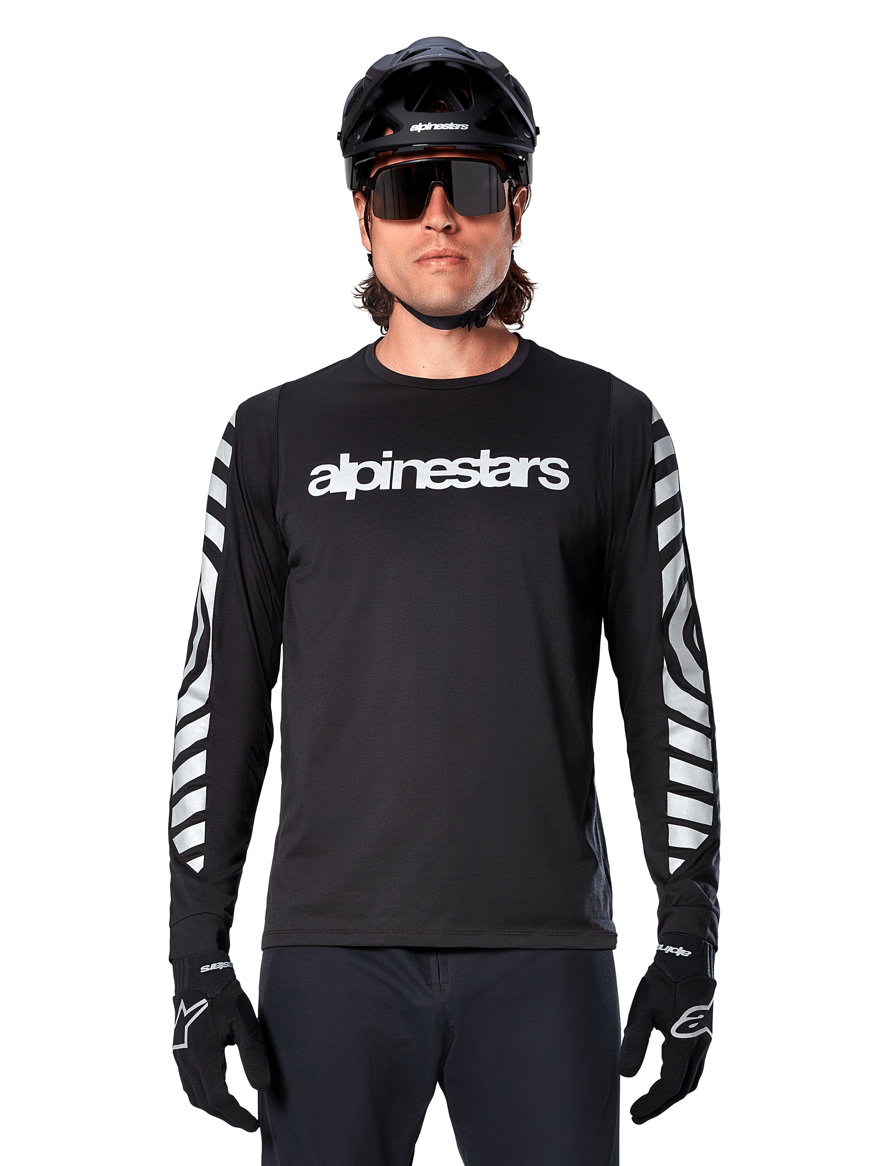 Ciclista masculino con jersey de manga larga Alpinestars A-Dura Dri Oscar, Negro Reflectante, con logotipo de Alpinestars en blanco en el pecho y gráficos reflectantes plateados en las mangas, combinado con casco de MTB negro, gafas de sol y guantes negros, equipamiento de ciclismo de alto rendimiento