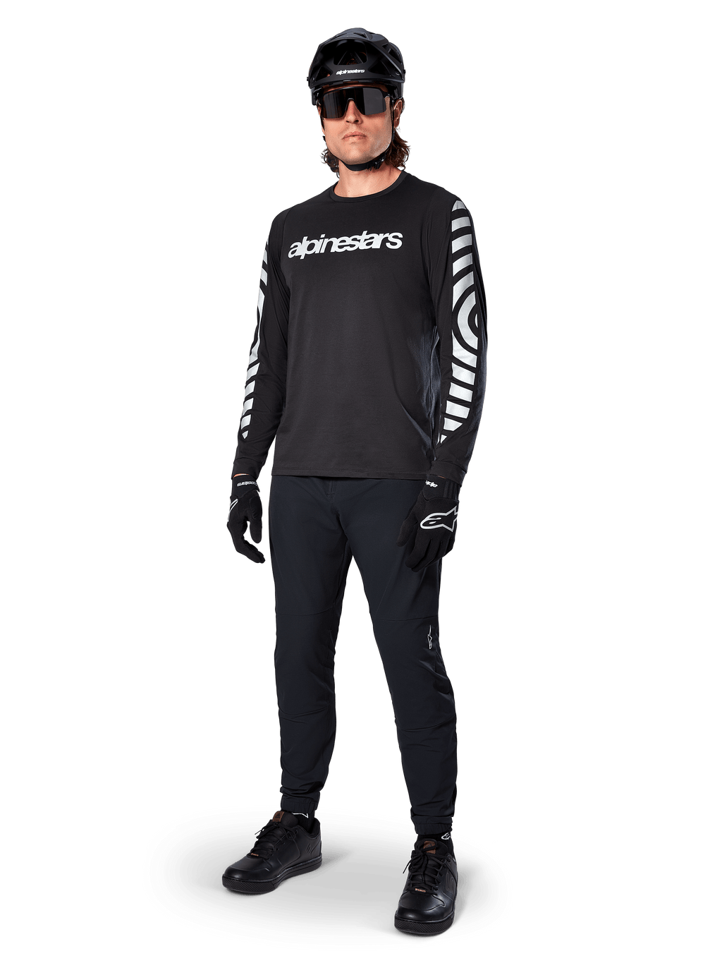 Jersey de manga larga Alpinestars A-Dura Dri Oscar, negro reflectante, con el logotipo de Alpinestars en blanco en el pecho y patrones gráficos reflectantes en las mangas, combinado con pantalones negros de ciclismo de montaña, casco y guantes, ropa técnica de MTB