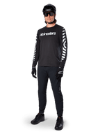 Jersey de manga larga Alpinestars A-Dura Dri Oscar, negro reflectante, con el logotipo de Alpinestars en blanco en el pecho y patrones gráficos reflectantes en las mangas, combinado con pantalones negros de ciclismo de montaña, casco y guantes, ropa técnica de MTB