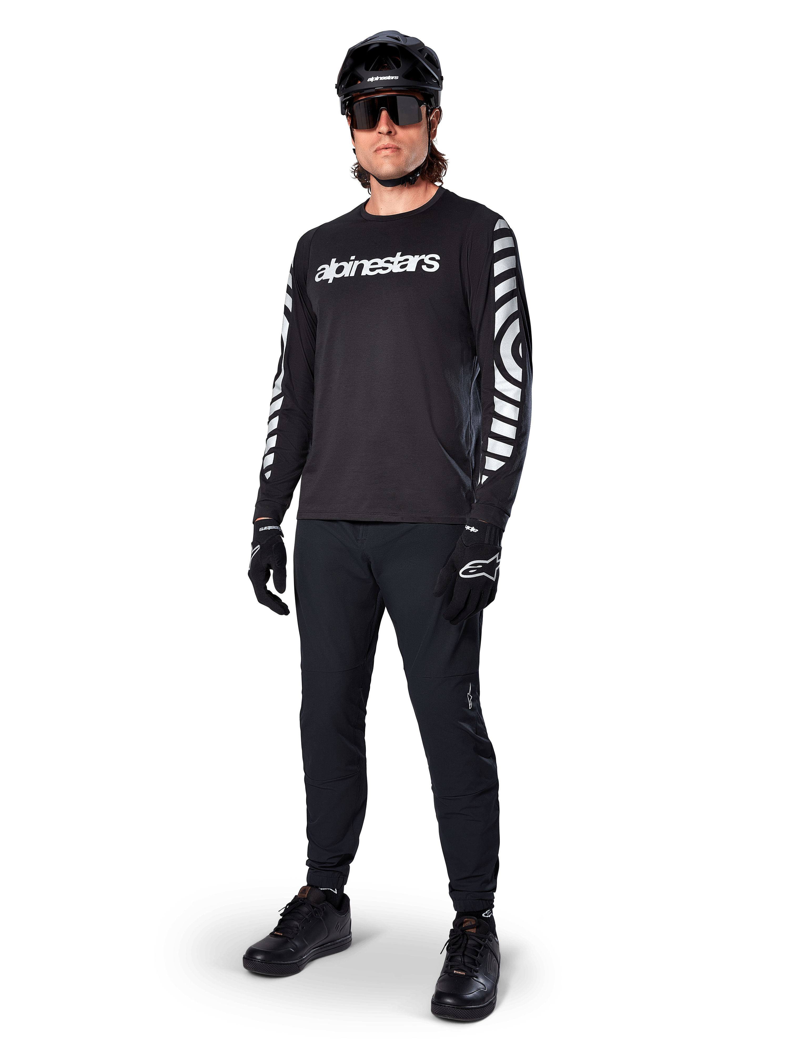 Jersey de manga larga Alpinestars A-Dura Dri Oscar, negro reflectante, con el logotipo de Alpinestars en blanco en el pecho y patrones gráficos reflectantes en las mangas, combinado con pantalones negros de ciclismo de montaña, casco y guantes, ropa técnica de MTB