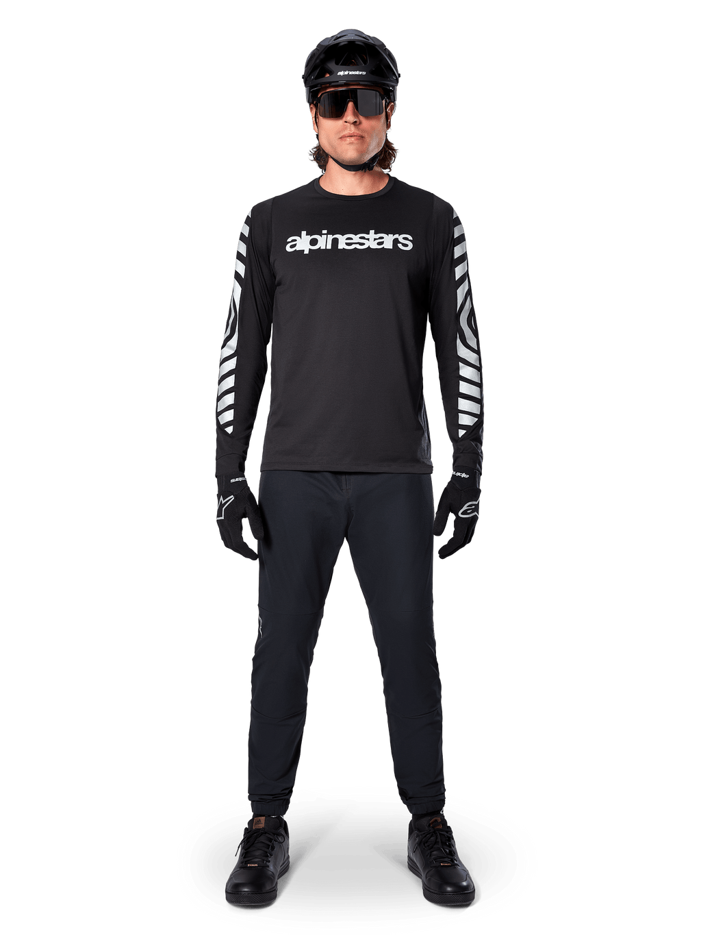 Alpinestars A-Dura Dri Oscar Long Sleeve Jersey en Negro Reflectante, usado con casco negro y gafas de sol, con logotipo blanco en el pecho y patrones gráficos reflectantes en las mangas, equipamiento de MTB para ciclismo de montaña