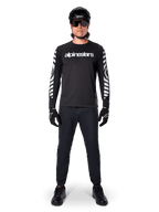 Alpinestars A-Dura Dri Oscar Long Sleeve Jersey en Negro Reflectante, usado con casco negro y gafas de sol, con logotipo blanco en el pecho y patrones gráficos reflectantes en las mangas, equipamiento de MTB para ciclismo de montaña