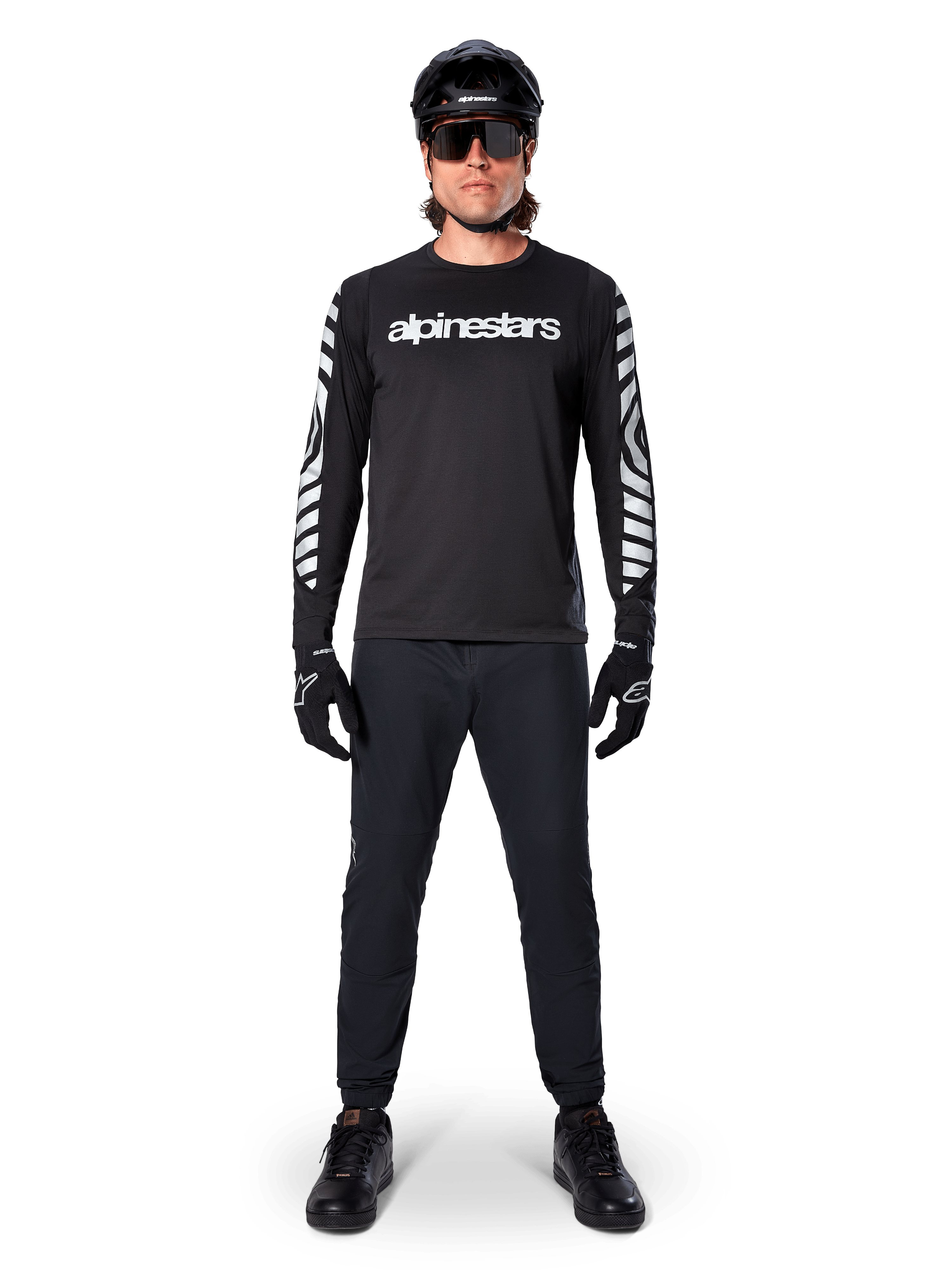 Alpinestars A-Dura Dri Oscar Long Sleeve Jersey en Negro Reflectante, usado con casco negro y gafas de sol, con logotipo blanco en el pecho y patrones gráficos reflectantes en las mangas, equipamiento de MTB para ciclismo de montaña