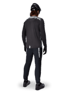 Ciclista de montaña vistiendo el Jersey de Manga Larga Alpinestars A-Dura Dri Oscar en Negro Reflectante, visto desde atrás, combinado con pantalones técnicos negros, casco y guantes, con gráficos de rayas reflectantes en los hombros y una parte trasera más larga para ciclismo de montaña.