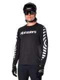 Alpinestars A-Dura Dri Oscar Jersey de manga larga, jersey de ciclismo MTB, negro reflectante, con logotipo blanco en el pecho y llamativos gráficos circulares reflectantes en las mangas, usado con casco negro y gafas de sol, prenda técnica transpirable para ciclismo de montaña