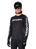 Alpinestars A-Dura Dri Oscar Jersey de manga larga, jersey de ciclismo MTB, negro reflectante, con logotipo blanco en el pecho y llamativos gráficos circulares reflectantes en las mangas, usado con casco negro y gafas de sol, prenda técnica transpirable para ciclismo de montaña