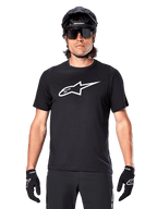 Alpinestars A-Dura Dri Oscar Jersey - Manga Corta, negro reflectante, usado con casco de MTB negro, gafas de sol y guantes, con un logotipo blanco prominente en el pecho, equipamiento de alto rendimiento para ciclismo de montaña