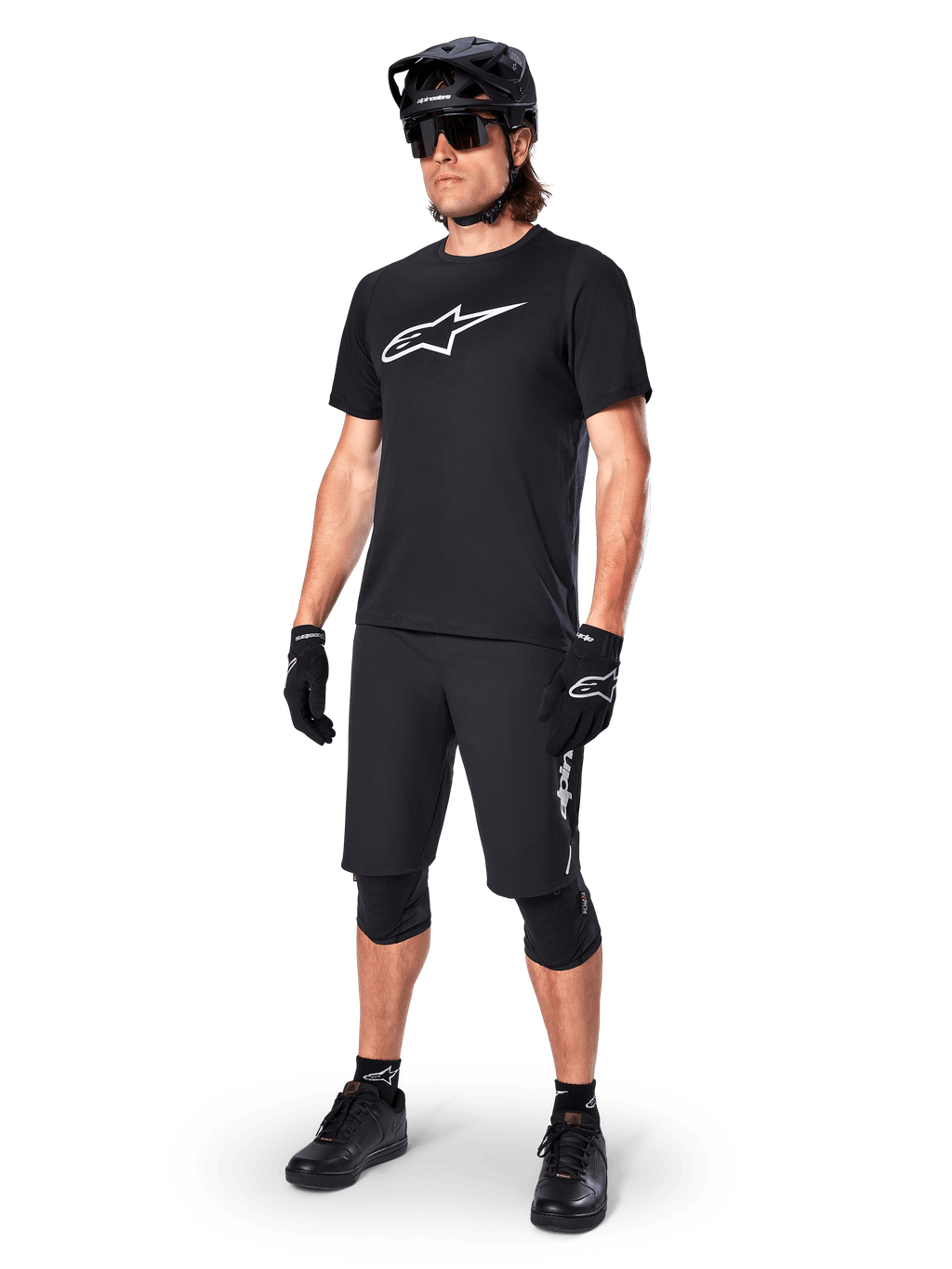 Ciclista de montaña con el Jersey de manga corta Alpinestars A-Dura Dri Oscar en Negro Reflectante, con un gran logotipo blanco en el pecho, combinado con pantalones cortos de MTB, guantes y casco negros a juego, ropa técnica de ciclismo para rendimiento off-road