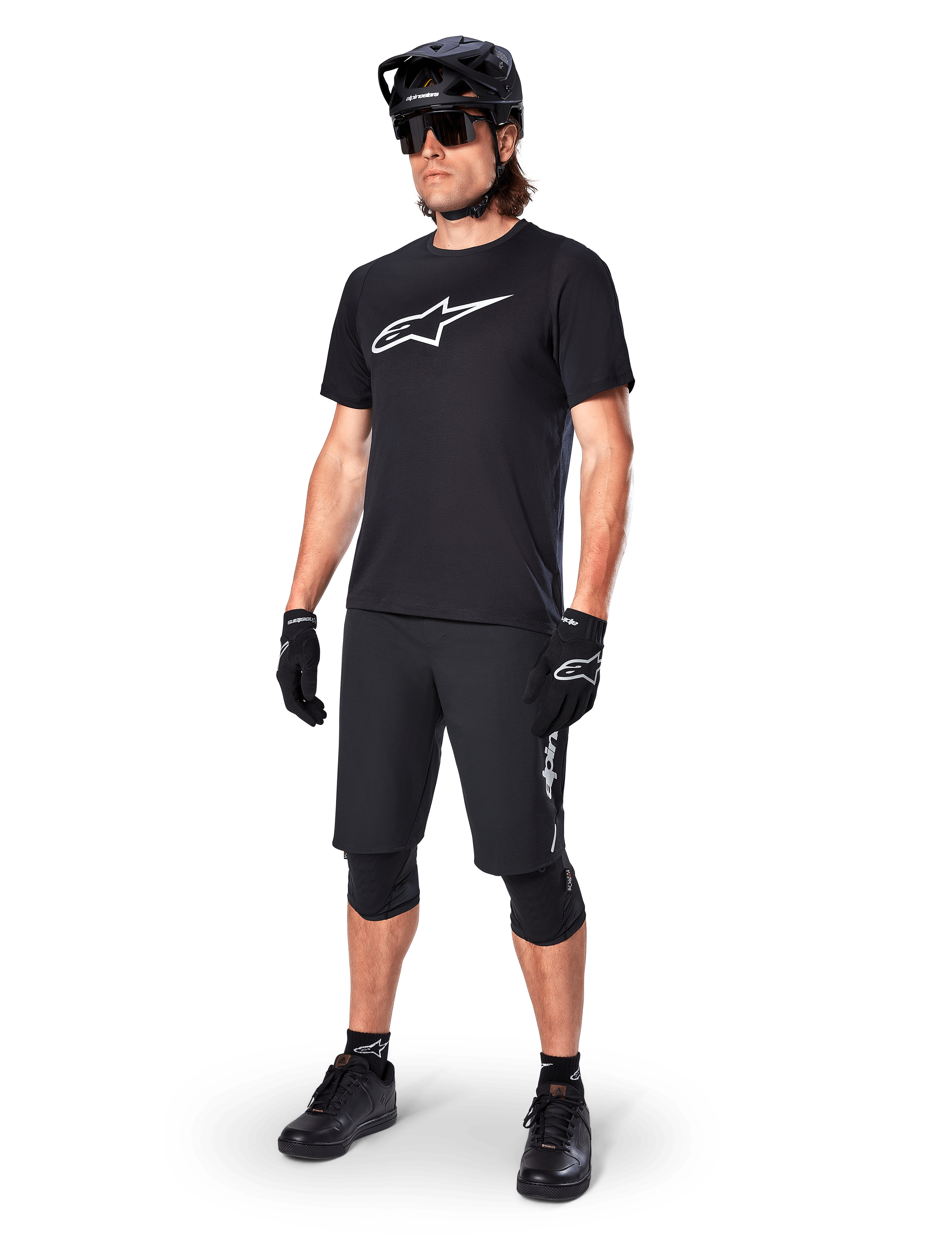 Ciclista de montaña con el Jersey de manga corta Alpinestars A-Dura Dri Oscar en Negro Reflectante, con un gran logotipo blanco en el pecho, combinado con pantalones cortos de MTB, guantes y casco negros a juego, ropa técnica de ciclismo para rendimiento off-road