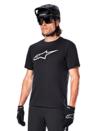 Alpinestars A-Dura Dri Oscar Jersey, camiseta de ciclismo MTB de manga corta, negra con logotipo blanco, tejido técnico transpirable, usada con casco negro, gafas de sol y guantes
